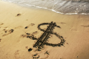 Conceptual image of close up dollar sign drawing on golden color sandy beach during dusk